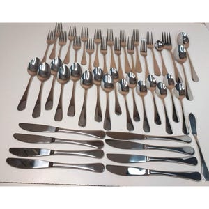May include: A large collection of stainless steel flatware including numerous forks, spoons, and knives. The set features a polished silver finish with simple, smooth handles. The pieces are arranged in rows, showcasing a variety of dinner forks, salad forks, soup spoons, teaspoons, dinner knives, and a single butter spreader.