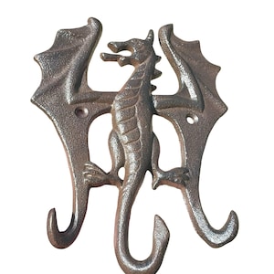 Puede incluir: Un gancho de pared con forma de dragón de color bronce. El dragón tiene alas detalladas y una cola larga y curvada. El gancho está diseñado con dos ganchos curvos y una figura central de dragón, ideal para colgar objetos.