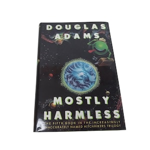 Könnte beinhalten: Ein Buchcover mit schwarzem Hintergrund und einer grünen Alienfigur. Der Titel des Buches lautet "Mostly Harmless" von Douglas Adams. Der Untertitel lautet "Das fünfte Buch der zunehmend ungenau benannten Anhalter-durch-die-Galaxis-Trilogie."