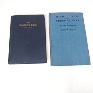 May include: Two hardcover books by Carl H. Claudy. The dark blue book is titled The Master's Book. The light blue book is titled Introduction to Freemasonry: Entered Apprentice. Both books feature gold or dark lettering on their front covers.