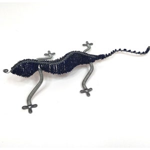 May include: A blue beaded wire gecko sculpture. The gecko is posed in a walking position with its tail curled up. The sculpture is made of wire and beads.