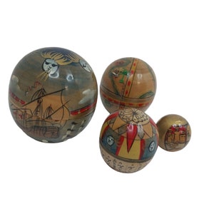 Puede incluir: Cuatro adornos de madera en forma de globo con diseños pintados a mano. El globo más grande presenta un barco y nubes, el segundo más grande tiene un mapa, el tercero tiene una brújula y rayas, y el más pequeño tiene un patrón geométrico.