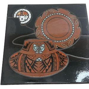 May include: Square ceramic tile with a black background featuring a Southwestern design. The design includes a brown pot with a butterfly, a plate, and a stylized face. The tile is approximately 8 inches square.