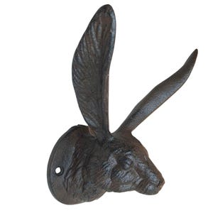 Könnte beinhalten: Ein dunkelbrauner, texturierter Wandhaken aus Gussmetall in Form eines Hasenkopfes. Der Hase hat lange, aufrechte Ohren und eine kreisförmige Montageplatte mit einem sichtbaren Schraubloch auf der linken Seite, konzipiert für die Wandmontage.