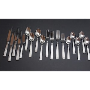 May include: A collection of stainless steel flatware featuring five knives, four forks, and seven spoons. Each piece has a polished finish and a handle decorated with vertical ridges. The set is arranged in a row against a dark background.