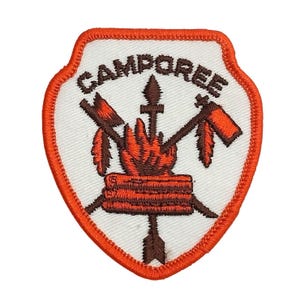 Może przedstawiać: Naszywka haftowana na pomarańczowo z napisem "CAMPOREE" w brązowych literach. Naszywka przedstawia ognisko z krzyżującymi się siekierami i strzałami.