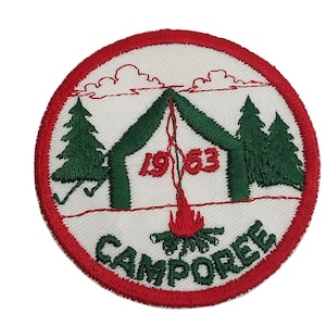 Puede incluir: Un parche redondo blanco bordado con un borde rojo. El parche presenta una tienda de campaña verde con una fogata roja debajo. El año 1963 está bordado en rojo sobre la fogata. Las palabras "CAMPOREE" están bordadas en verde alrededor de la parte inferior del parche.