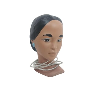 May include: A ceramic bust of a woman with dark hair, brown skin, and blue earrings. She is wearing a silver necklace.