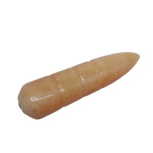 May include: A light peach-colored, elongated stone with a rounded end and a pointed tip. The stone has a smooth, polished surface and appears to be a natural gemstone or crystal. The shape is similar to a bullet or a wand.