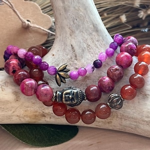 May include: Three layered bracelets with pink, purple, and red agate beads. The bracelets feature a Buddha charm and a lotus flower charm.