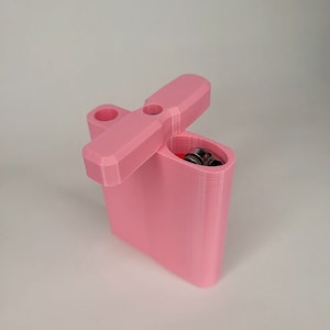 May include: A pink 3D printed container with a hinged lid. The lid has a small handle on top. The container is open and a silver lighter is inside.