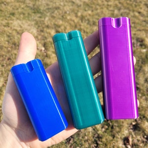 May include: Three small rectangular containers in blue, green, and purple. The containers have a smooth, textured surface and a small opening at the top.