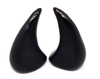 Könnte beinhalten: Ein Paar schwarze Teufelshörner aus Kunststoff. Die Hörner sind spitz und haben eine glatte Oberfläche.