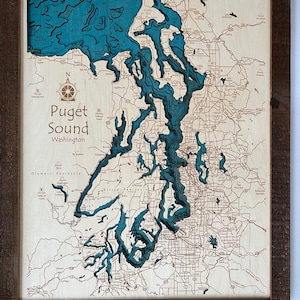 May include: A wooden map of Puget Sound, Washington, with a teal blue color representing the water. The map is framed in a rustic brown wood frame.