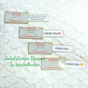 Puede incluir: Una colección de pines de esmalte con forma de sobres con bordes dorados. Cada pin presenta la palabra "OFICIAL" y "CORREO URGENTE". Las pancartas adjuntas dicen: "HEMOS ESTADO INTENTANDO CONTACTARLO...", "TE AMO", "JÓDETE" y "TE EXTRAÑO".