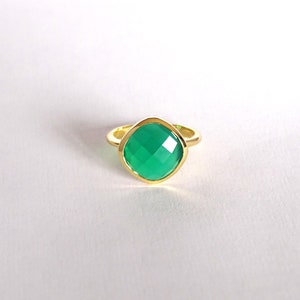 Puede incluir: Un anillo de oro con una piedra preciosa verde. El anillo tiene una forma cuadrada y un acabado liso y pulido.