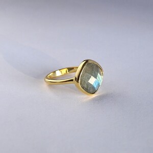 May include: A gold ring with a large, faceted, gray labradorite gemstone. The ring is set in a simple, modern style.