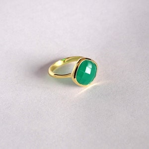 Puede incluir: Un anillo de oro con una piedra preciosa verde. La piedra preciosa es de forma cuadrada con bordes redondeados y tiene un corte facetado.