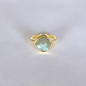 May include: A gold ring with a light blue labradorite gemstone. The ring is set in a simple band.