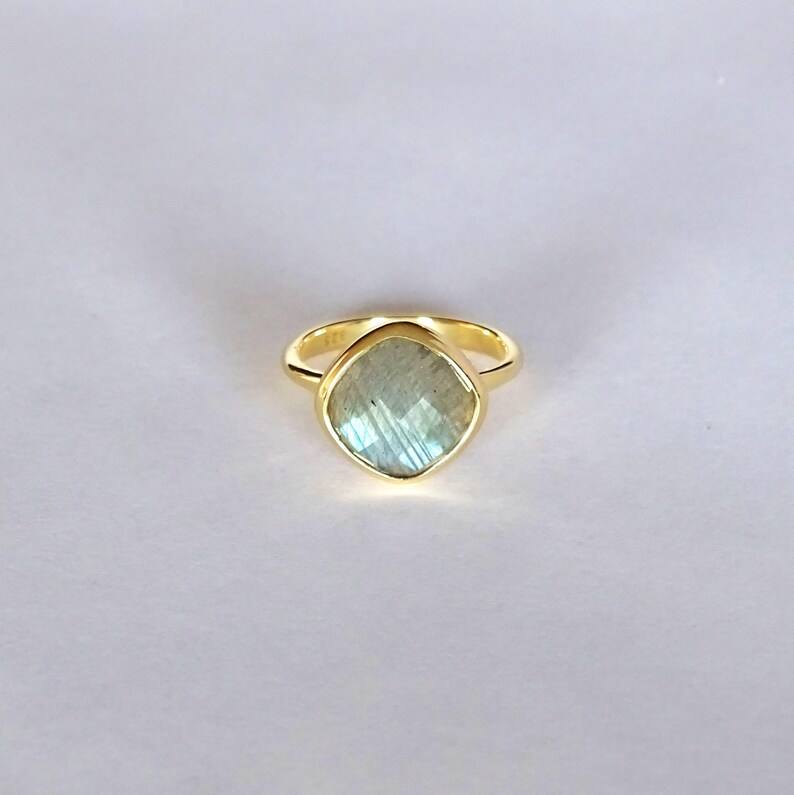 May include: A gold ring with a light blue labradorite gemstone. The ring is set in a simple band.