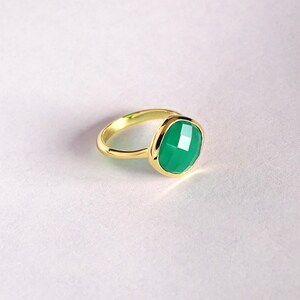 Puede incluir: Un anillo de oro con una piedra preciosa verde. La piedra preciosa es de talla coj&iacute;n y tiene un dise&ntilde;o facetado.