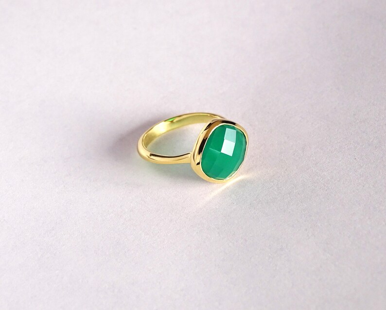 Puede incluir: Un anillo de oro con una piedra preciosa verde. La piedra preciosa es de talla coj&iacute;n y tiene un dise&ntilde;o facetado.