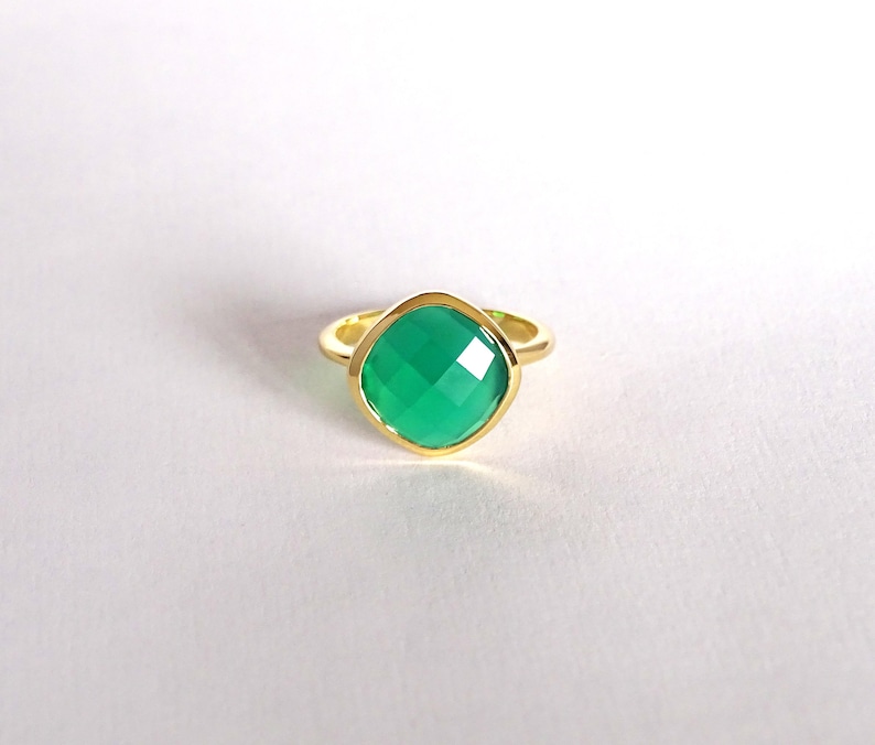 Puede incluir: Un anillo de oro con una piedra preciosa verde. El anillo tiene una forma cuadrada y un acabado liso y pulido.