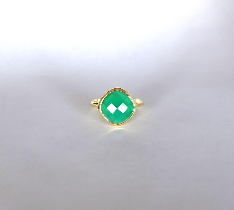 Puede incluir: Un anillo de oro con una piedra preciosa verde. La piedra preciosa es de talla coj&iacute;n y tiene un dise&ntilde;o facetado.