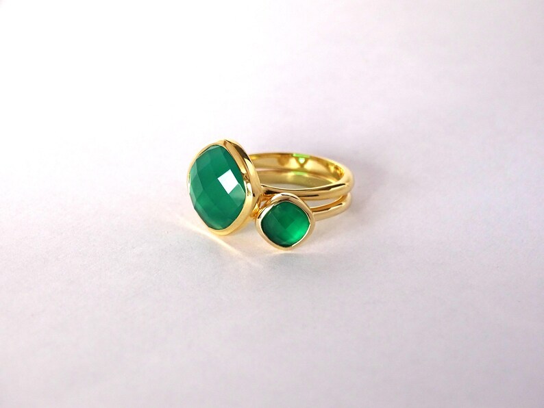 Puede incluir: Un anillo de oro con dos engastes de piedras preciosas verdes. La piedra m&aacute;s grande es de forma cuadrada y la m&aacute;s peque&ntilde;a es redonda.