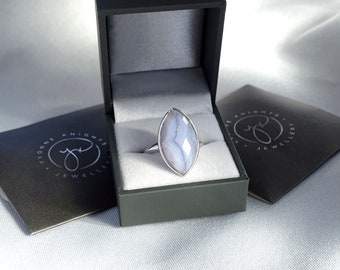 May include: A silver ring with a light blue agate gemstone in a marquise shape. The ring is in a gray box with the text "Yvonne Knights Jewellers" on the lid.