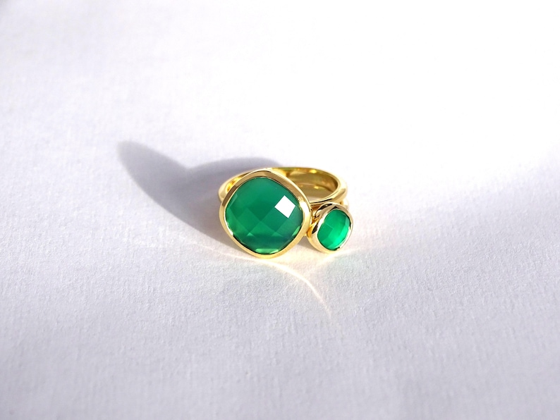 Puede incluir: Un anillo de oro con dos engastes de piedras preciosas verdes. La piedra m&aacute;s grande es de forma cuadrada, mientras que la m&aacute;s peque&ntilde;a es redonda.