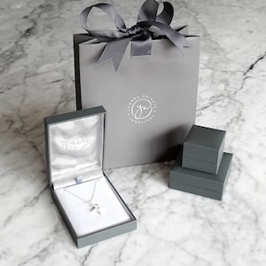 May include: A gray jewelry box with a silver necklace inside. The box has a logo that says "Yvonne Knight Jewellery". The necklace is in a gray gift bag with a gray ribbon.