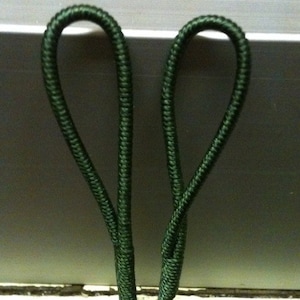 May include: Two green elastic loops, each forming a circle with a small opening at the top. The loops are connected at the bottom, creating a V-shape.