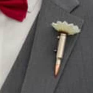 May include: A gray suit jacket with a white flower boutonniere made from a bullet casing. The boutonniere is pinned to the lapel of the jacket.