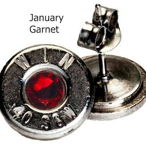 May include: A pair of silver bullet earrings with a red garnet gemstone in the center. The earrings are marked "WIN 40 S&W".
