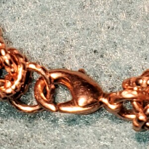 May include: A close-up of a rose gold chain bracelet with a lobster clasp closure. The chain is made of small, interconnected circles.