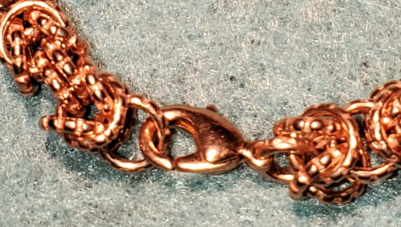 May include: A close-up of a rose gold chain bracelet with a lobster clasp closure. The chain is made of small, interconnected circles.