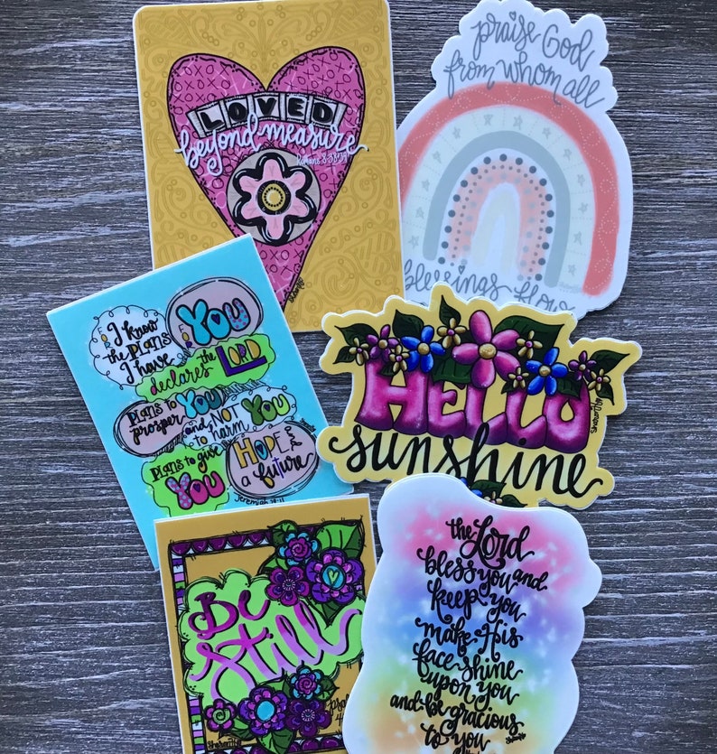 May include: Assortment of colorful stickers with inspirational quotes and designs. Stickers feature phrases like "Loved beyond measure", "I know the plans I have for you", "Be Still", "Hello Sunshine", and "The Lord bless you and keep you".