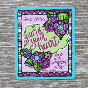 May include: A rectangular sticker with a teal border and a light purple background. The sticker features the words "guard your heart" in a whimsical font, surrounded by colorful flowers and the text "above all else, for it is the wellspring of life, Proverbs 4:23."