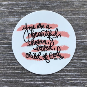 May include: A round white sticker with the words "You are a beautiful, chosen, loved, child of God" in black script. The text is overlaid on pink brushstrokes. Bible verses are also included.