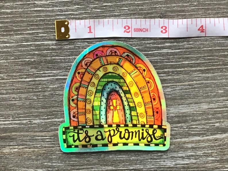 May include: A colorful rainbow sticker with a cross in the center and the text "it's a promise" below. The sticker is iridescent and has a holographic finish.