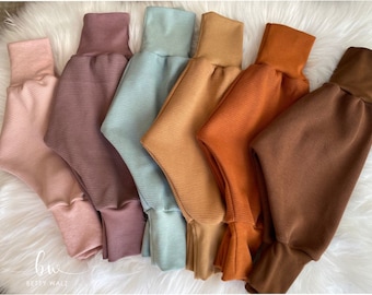 May include: A collection of six waffle-knit pants arranged side by side in a gradient of colors including light pink, mauve, sage green, tan, burnt orange, and dark brown. Each pair of pants features a solid-colored ribbed waistband and ankle cuffs.