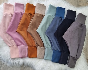 May include: A collection of eight pairs of soft, stretchy pants in various colors, including pink, orange, brown, light blue, dark blue, gray, and black. The pants have a gathered elastic waistband and cuffed legs.