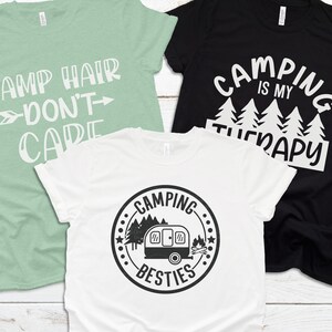 May include: Three t-shirts with camping-themed designs. The first shirt is light green with the text "Camp Hair Don't Care". The second shirt is black with the text "Camping is my Therapy". The third shirt is white with a black and white graphic of a camper and the text "Camping Besties".