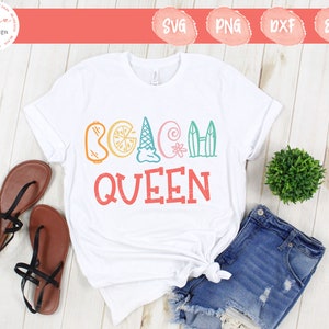 May include: White t-shirt with the words "BEACH QUEEN" in colorful, playful lettering. The design includes beach-themed icons like a slice of orange, ice cream cone, seashell, and surfboards. The shirt is paired with denim shorts and sandals.