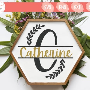 May include: A hexagonal wooden frame containing a white sign with a large black letter C, a gold script name Catherine, and black leaf branch accents. The design includes horizontal lines splitting the letter C and the name.