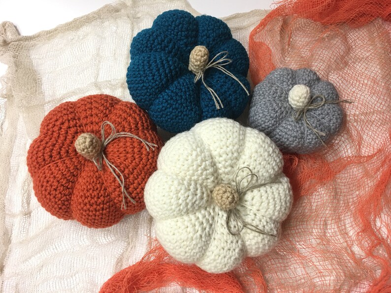 May include: Four crocheted pumpkins in different colors: teal, orange, white, and gray. Each pumpkin has a crocheted stem and a brown twine bow.