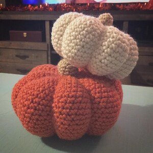 May include: A crocheted pumpkin with a white crocheted top. The pumpkin is orange and the top is white.