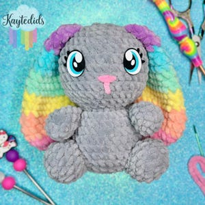 May include: A handmade gray plush bunny with large blue eyes, a pink nose, and rainbow-colored ears. The bunny is sitting on a blue surface. The text "Kaytedids" is in the upper left corner.
