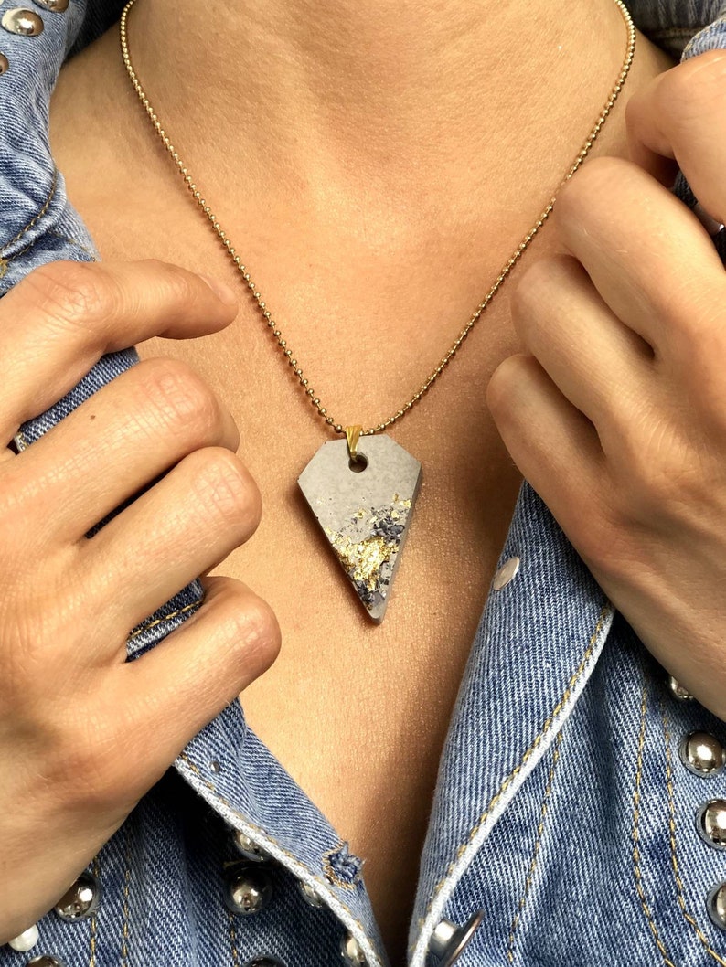 May include: A gold chain necklace with a gray concrete pendant featuring gold flecks. The pendant is shaped like a triangle with rounded edges.